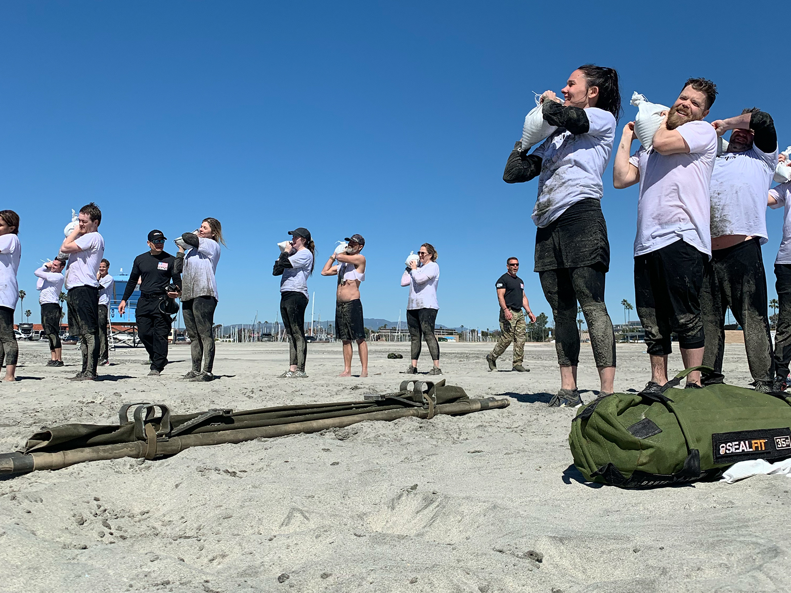 Qualia team carrying sandbags during SEAL Fit resilience training on the beach