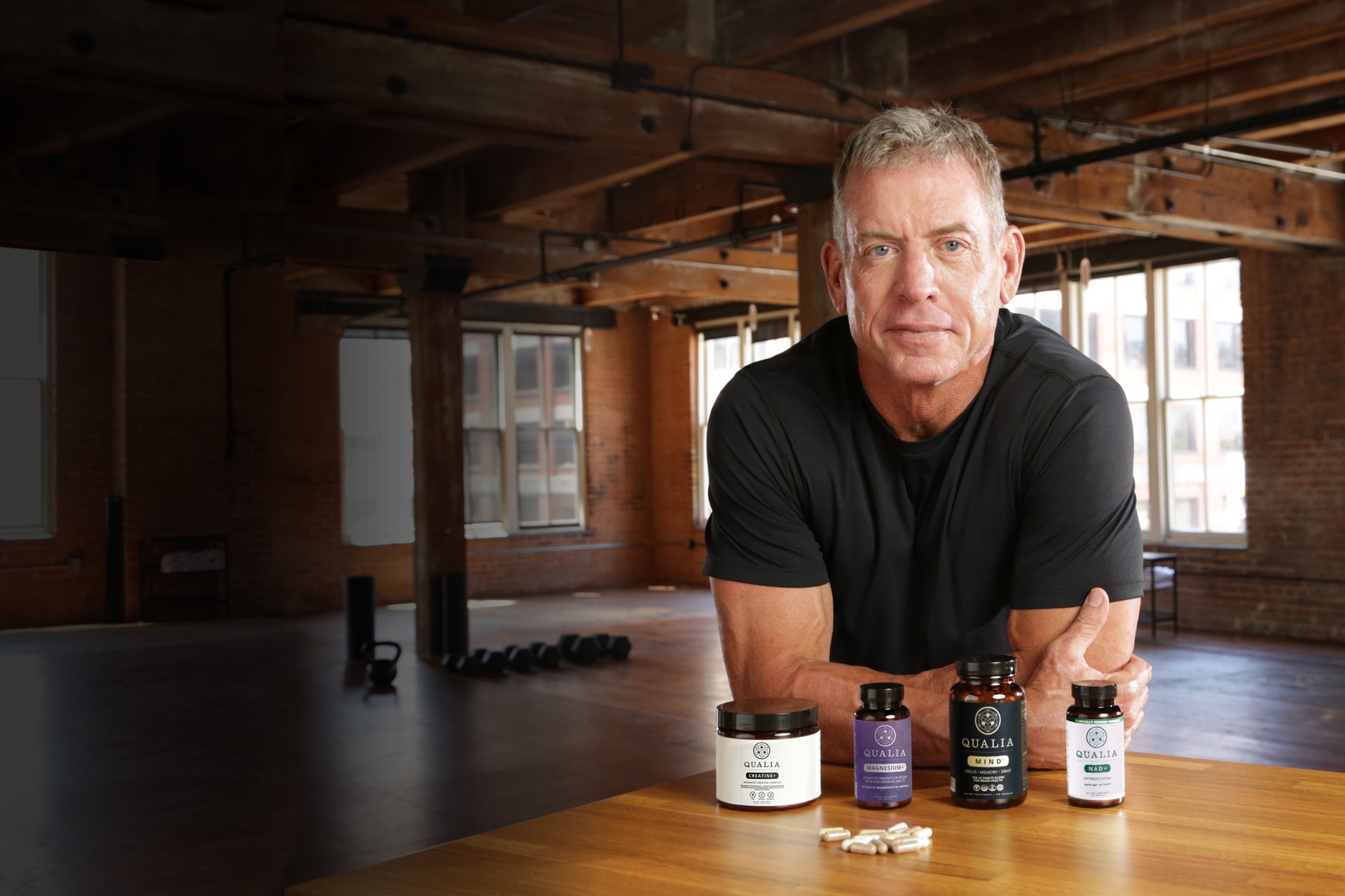 Troy Aikman leaning on a table with four Qualia products